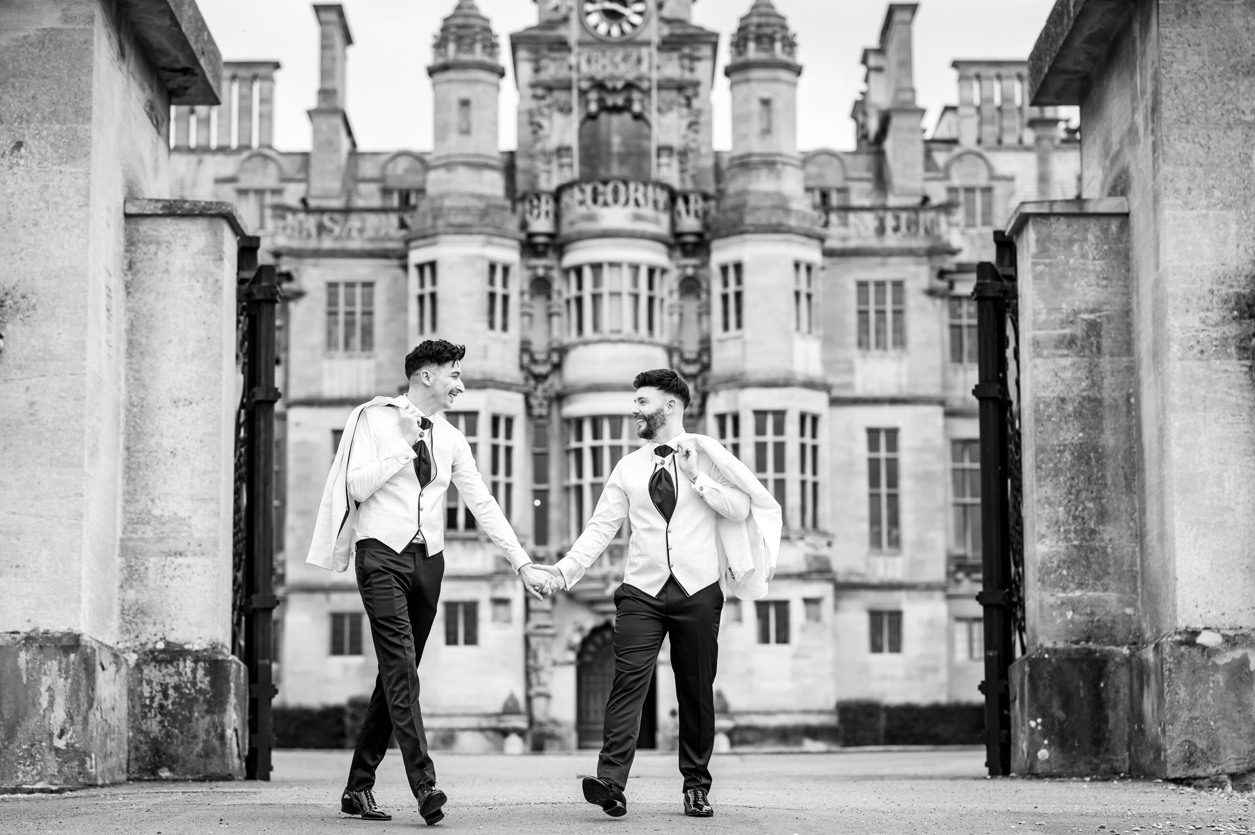 Grooms walking hand in hand outside Harlaxton Manor
